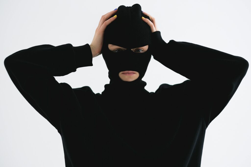 A person in a black balaclava with hands on head creates a mysterious and suspenseful vibe.
