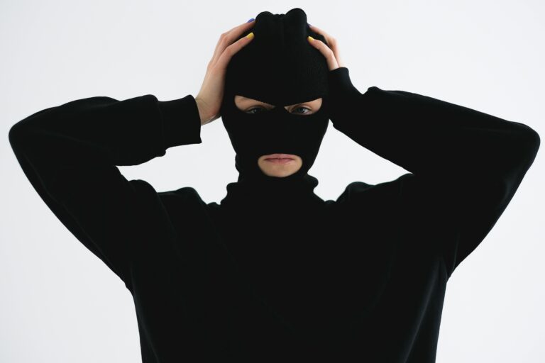 A person in a black balaclava with hands on head creates a mysterious and suspenseful vibe.